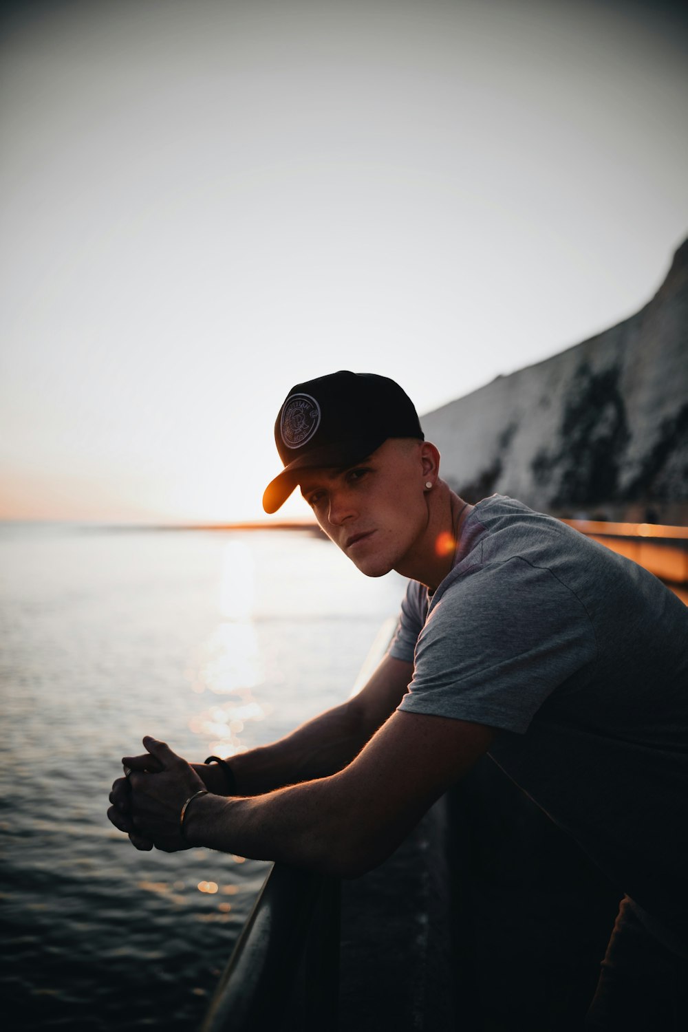 man in gray t-shirt and black cap standing near body of water during daytime