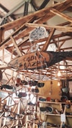 A wooden structure featuring shelves and hanging elements displays various handmade pottery and ceramics. The setup includes vibrant ceramic bowls, plates, and ornaments, with some pieces hanging. Natural lighting adds warmth to the scene.