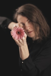 woman holding pink flower in dark room