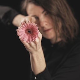 woman holding pink flower in dark room