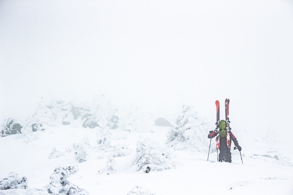 person in red jacket and black pants standing on snow covered ground during daytime