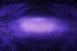 A vast, purple-hued galaxy filled with a multitude of stars spread across the dark expanse of space. The center of the galaxy is brighter, indicating dense star clusters, while the outer areas fade into a deeper purple and black, giving it a sense of depth and immensity.
