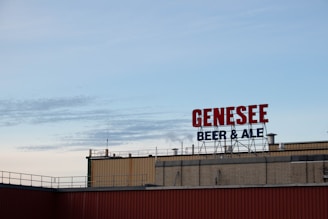 A rooftop display with large red letters spelling 'GENESEE' and smaller blue letters underneath spelling 'BEER & ALE' against a clear sky.
