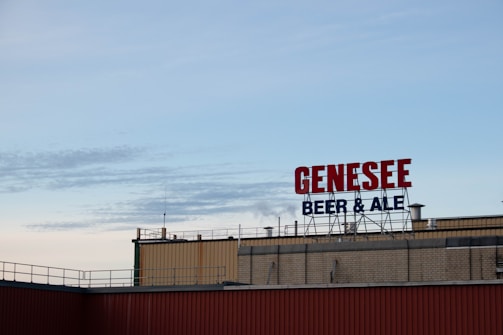 A rooftop display with large red letters spelling 'GENESEE' and smaller blue letters underneath spelling 'BEER & ALE' against a clear sky.