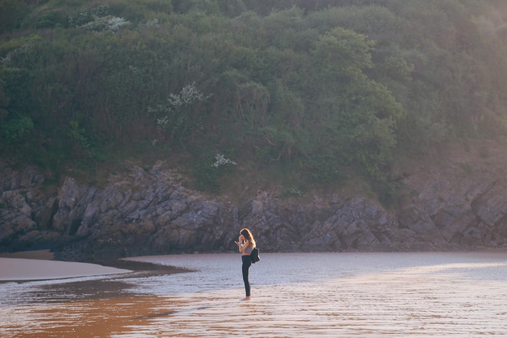 woman in black dress walking on brown sand near body of water during daytime