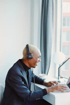 A smiling young woman with headphones taking notes during an online course.
