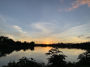 A serene landscape with a calm lake reflecting the sky at sunset.