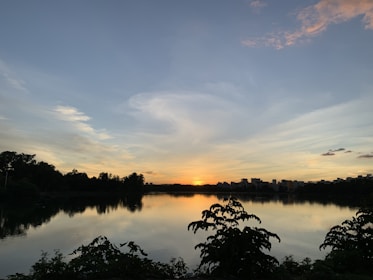 A serene landscape with a calm lake reflecting the sky at sunset.