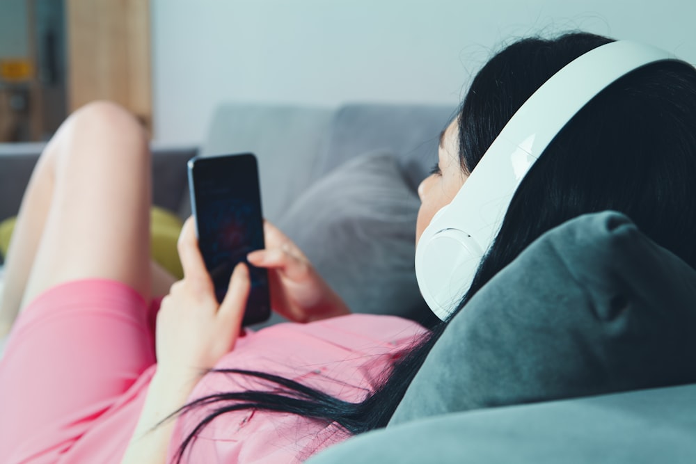 woman in pink shirt lying on bed holding smartphone