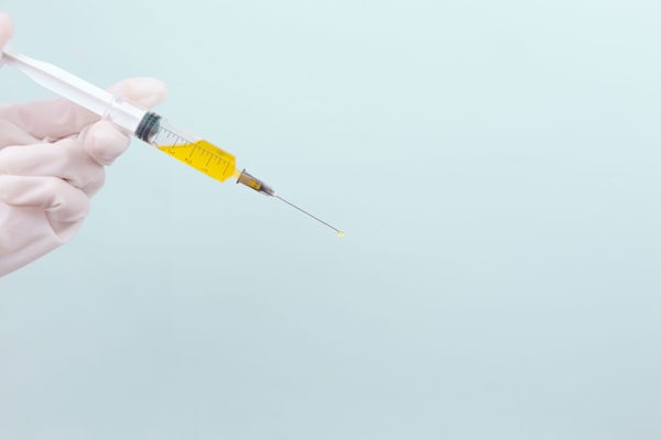 A gloved hand holding a needle full of yellow liquid.