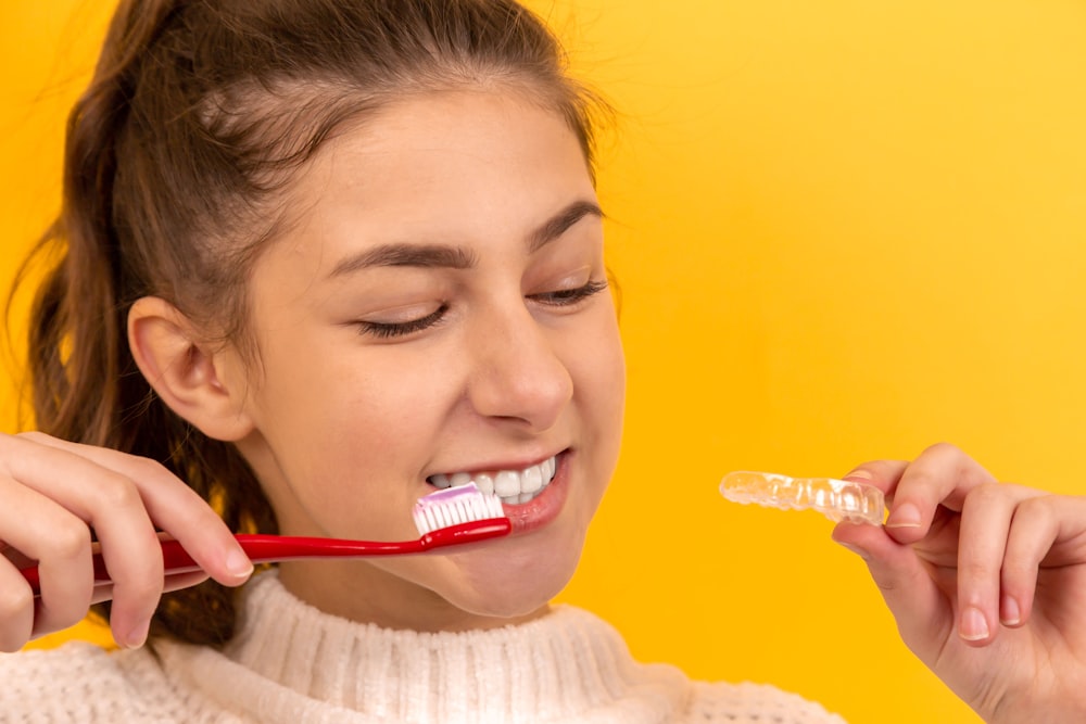 Chica sonriente en suéter blanco sosteniendo cepillo de dientes rojo y blanco