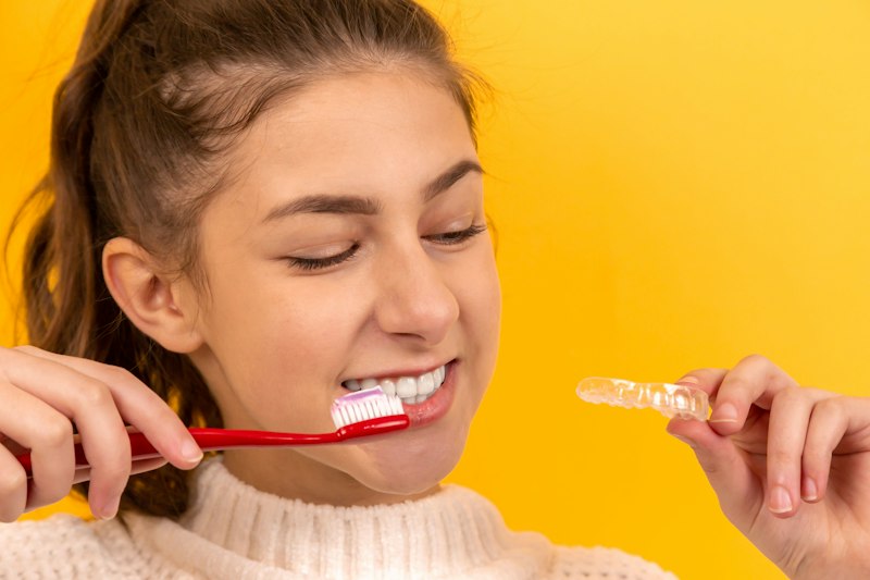 Adolescente escovando os dentes com alinhador na mão
