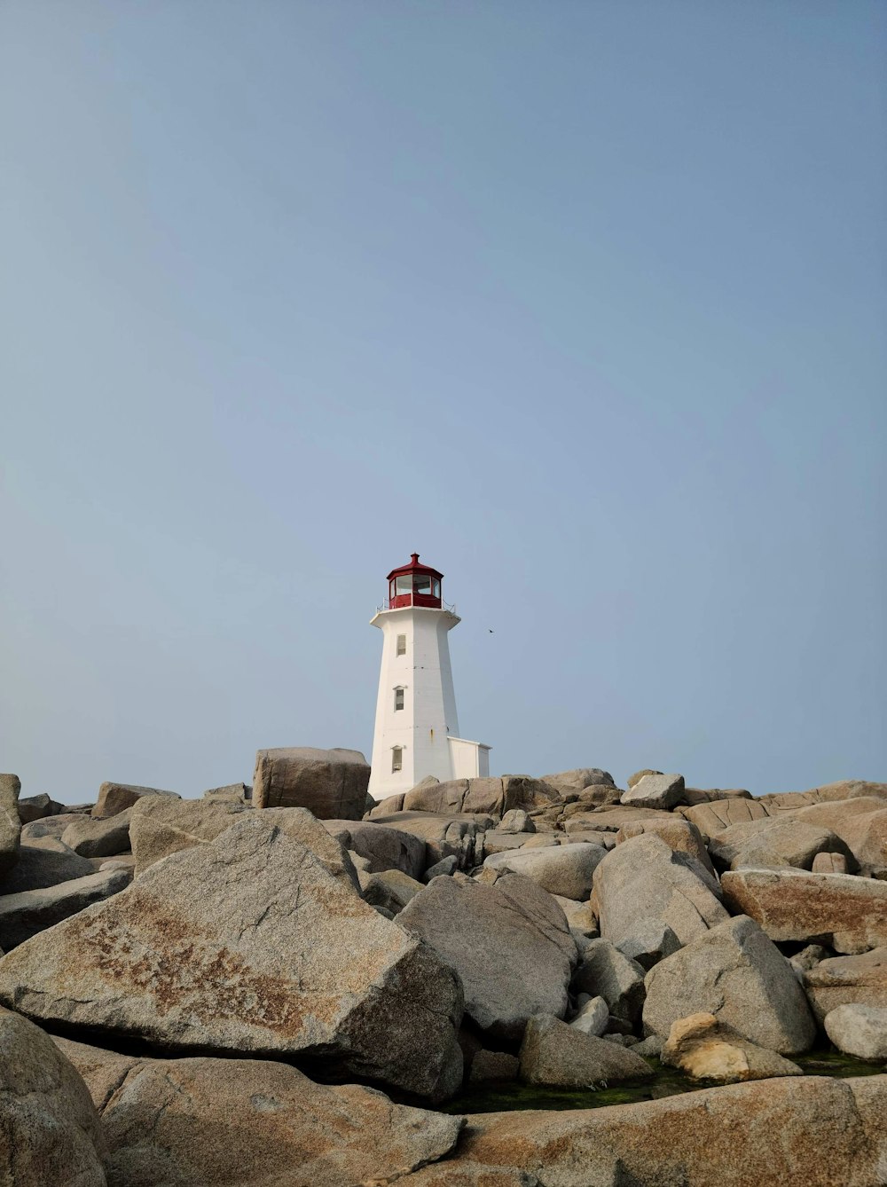 昼間の灰色の岩だらけの海岸にある白と赤の灯台