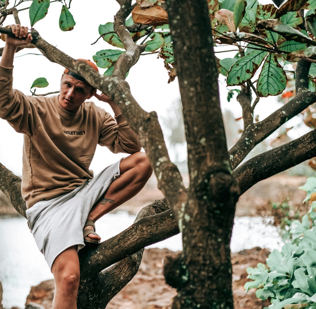 man in brown crew neck t-shirt and white shorts sitting on tree branch during daytime