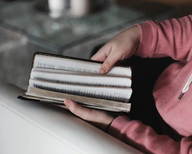 Hands holding a freshly printed book with soft pink cover on a wooden table.