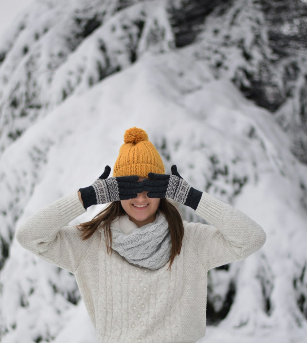 woman in white sweater wearing brown knit cap standing on snow covered ground during daytime