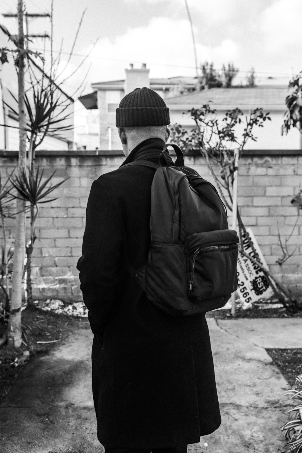 grayscale photo of man in black jacket and knit cap standing near wall