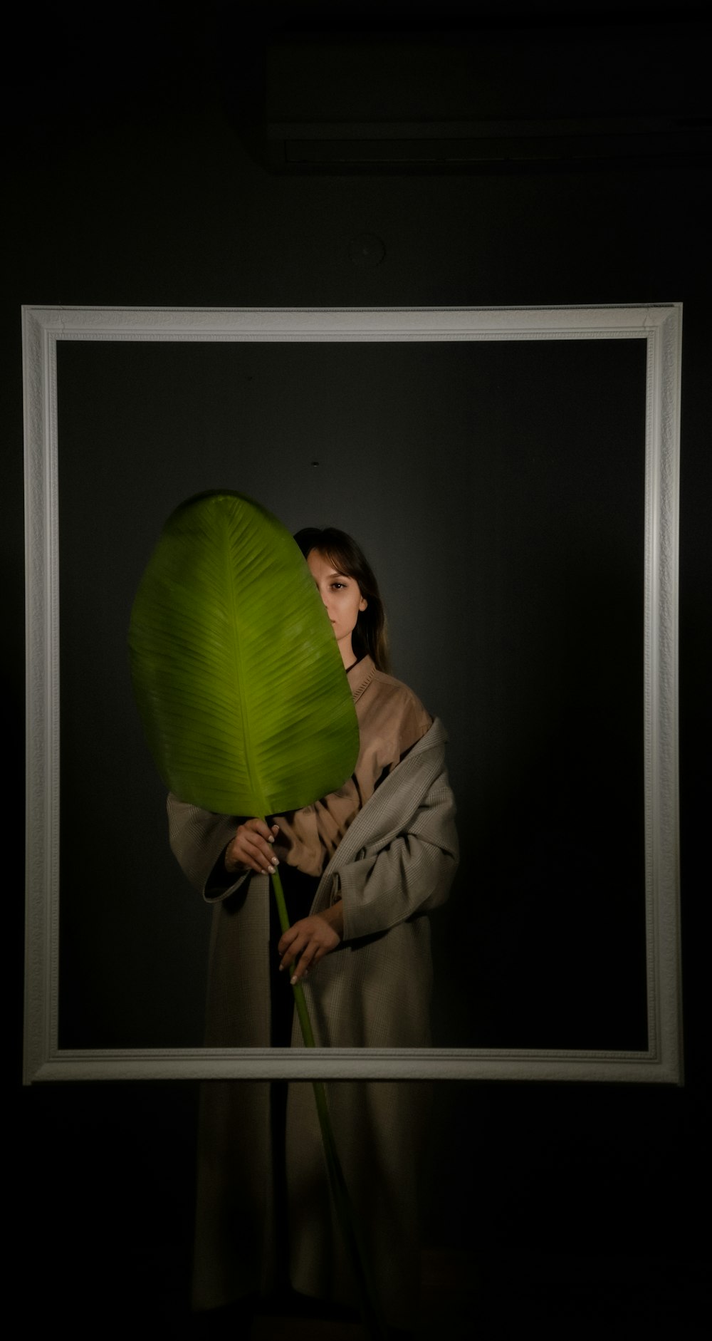 woman in gray coat covering face with green leaf