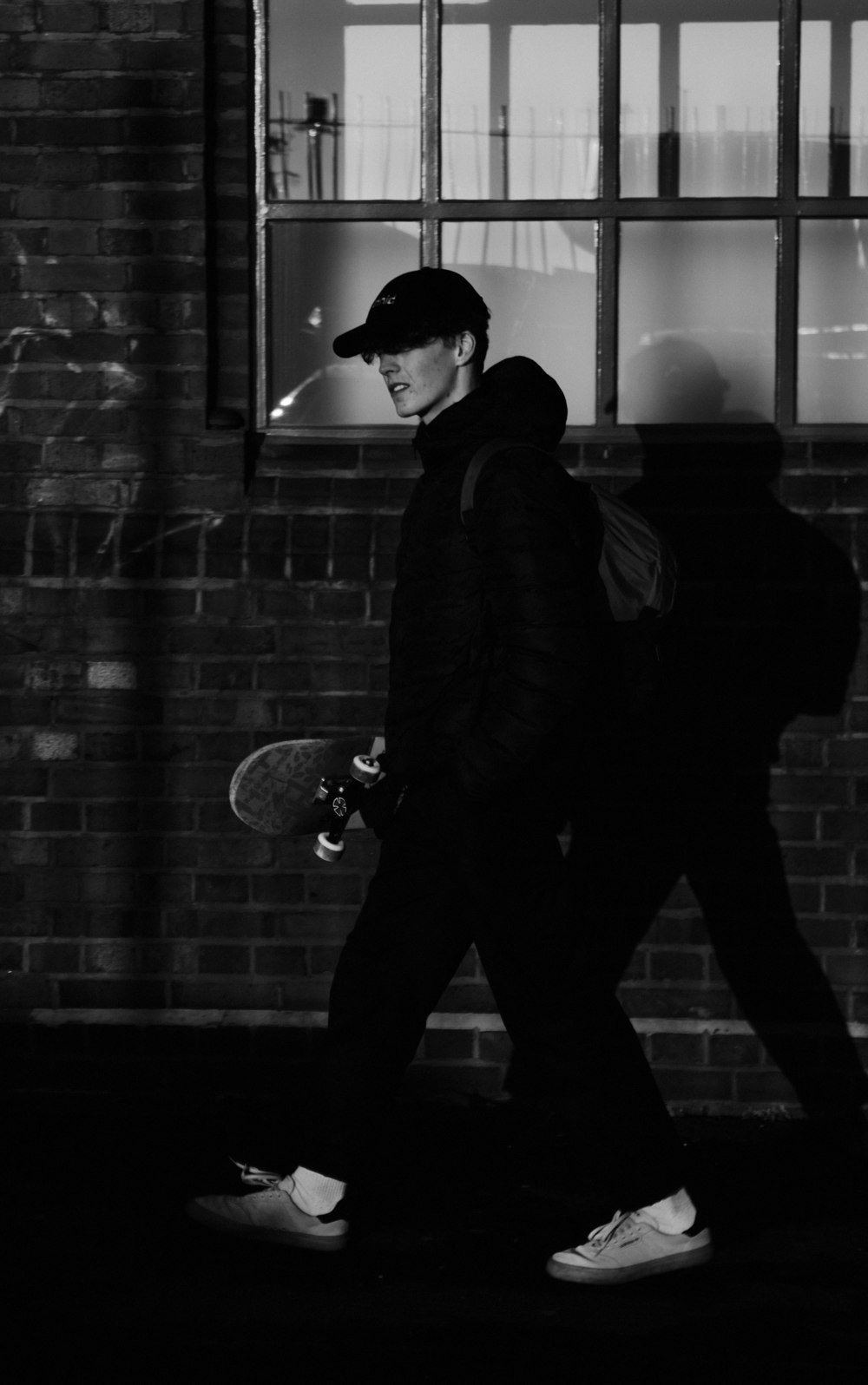 man in black jacket and black pants standing beside brick wall