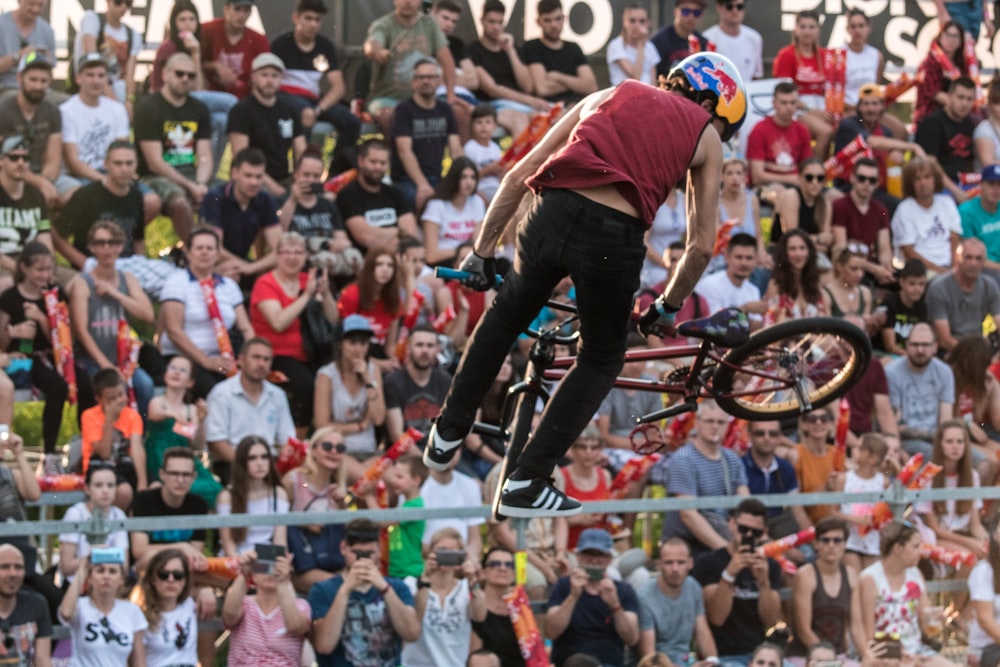 homem na camisa da camisa vermelha e branca e jeans azul andando na bicicleta bmx preta