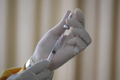 Gloved healthcare professional drawing medication from a vial into a syringe.