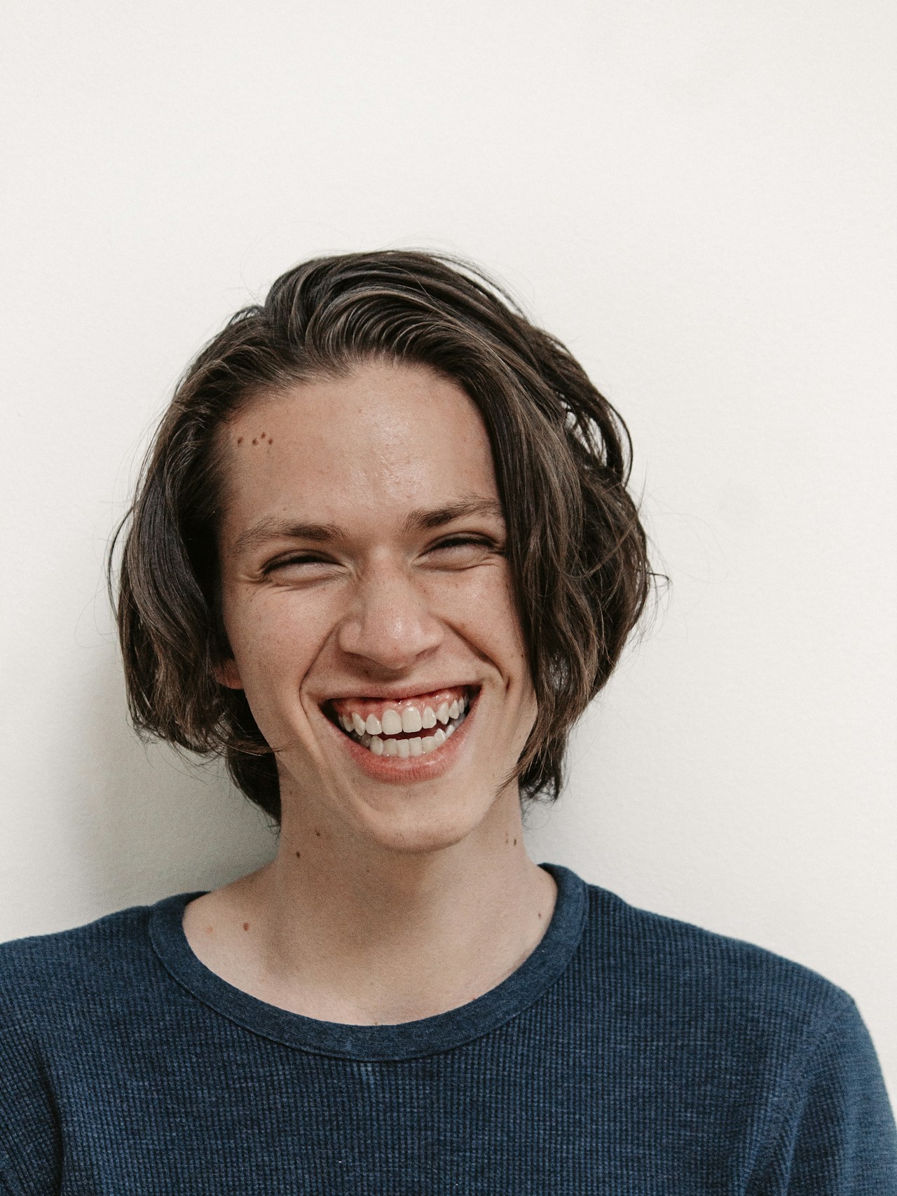 A person with shoulder-length brown hair laughing in a blue textured shirt