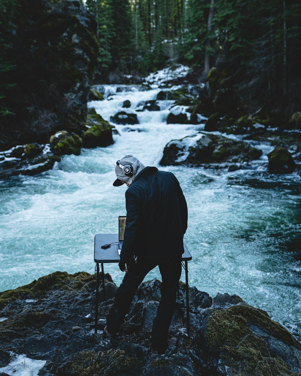 Homme en veste noire et casque blanc debout sur un rocher près de la rivière pendant la journée