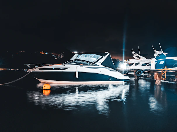 A modern motor boat docked at a marina with reflections shimmering on the water.