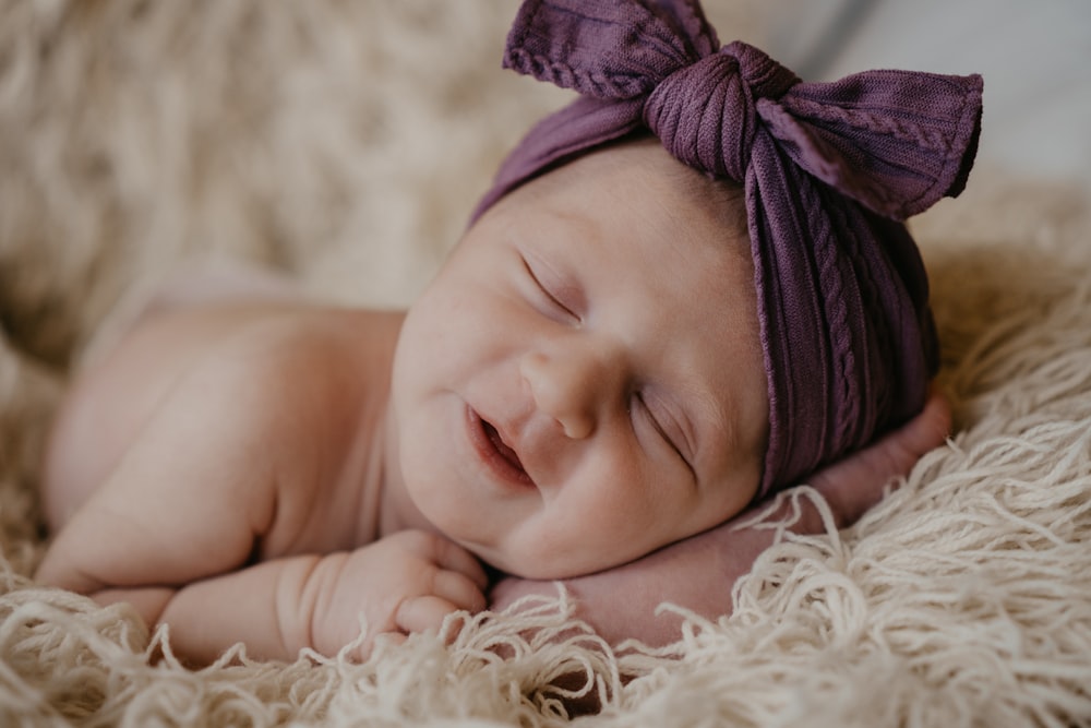 bambino in berretto a maglia viola sdraiato su tessuto di pelliccia bianca