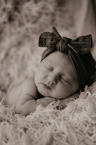 Smiling baby wearing a pastel blue bow headband sitting on a cozy blanket