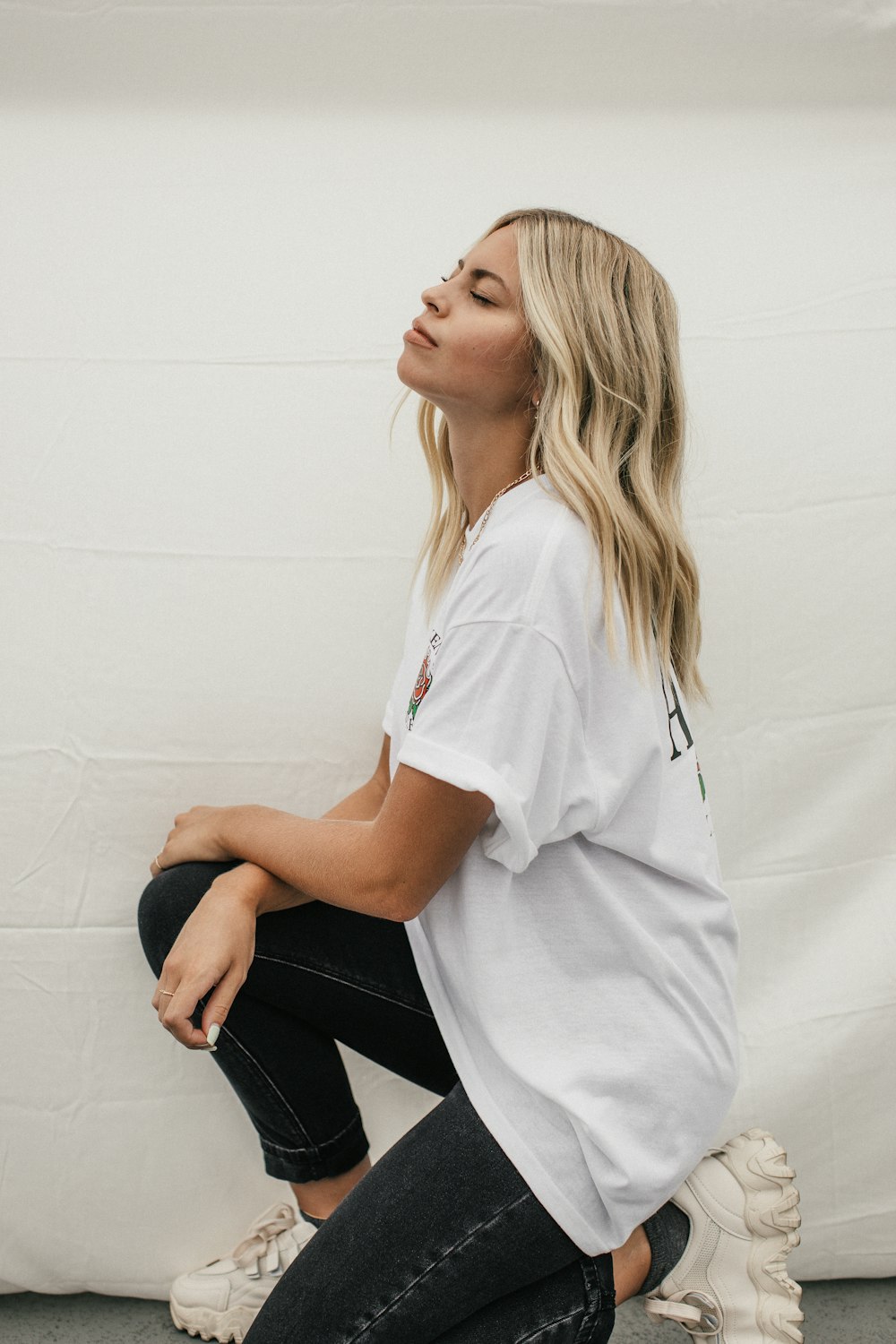 woman in white t-shirt and black pants sitting on white concrete wall