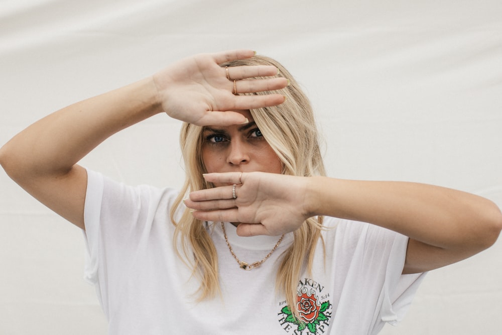 woman in white crew neck t-shirt covering her face with her hands