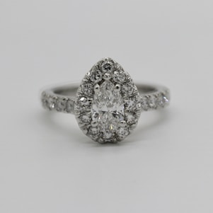 A pear-shaped diamond engagement ring features a central pear-cut diamond surrounded by smaller round diamonds. The band is also adorned with a line of sparkling diamonds, providing an elegant and luxurious appearance.