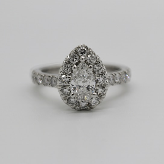 A pear-shaped diamond engagement ring features a central pear-cut diamond surrounded by smaller round diamonds. The band is also adorned with a line of sparkling diamonds, providing an elegant and luxurious appearance.