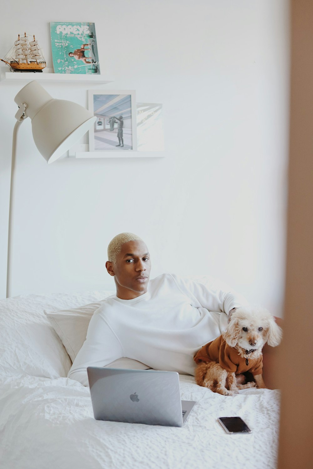man in white crew neck t-shirt sitting on bed beside brown short coated dog