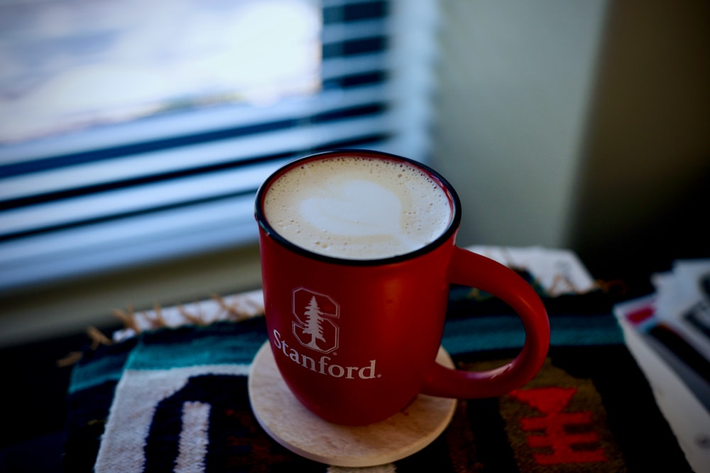 Tasse en céramique Nescafé rouge et blanc sur dessous de verre en bois marron