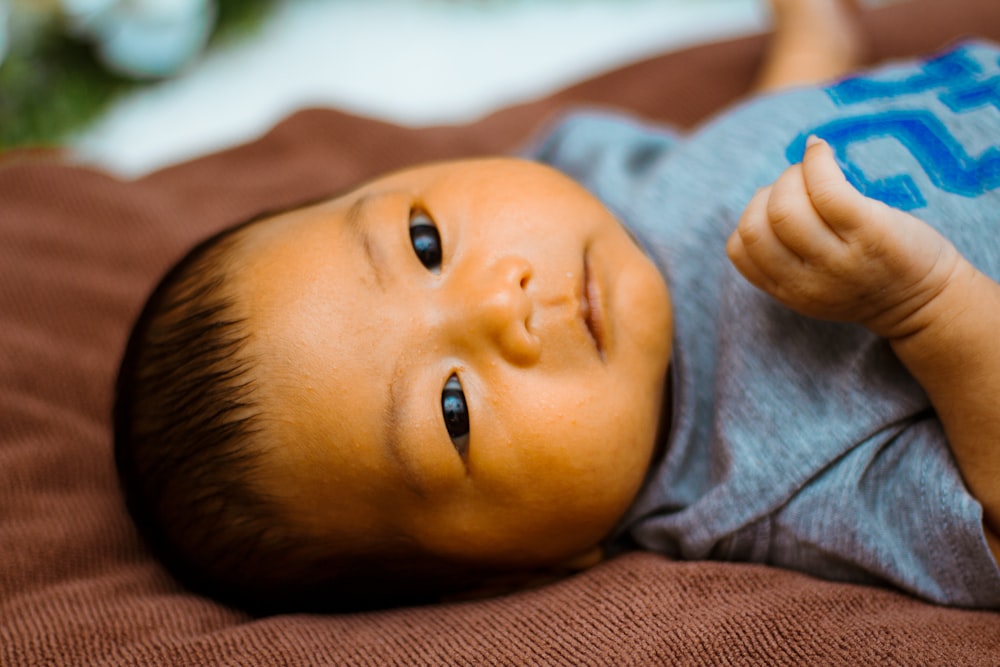 baby in gray shirt lying on brown textile