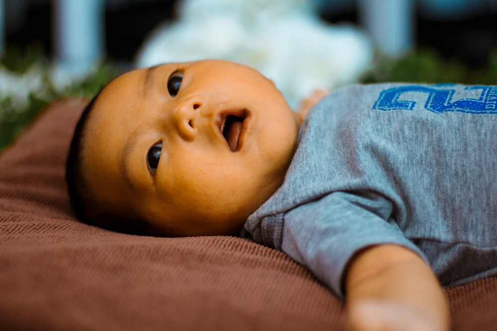 baby in gray shirt lying on brown textile