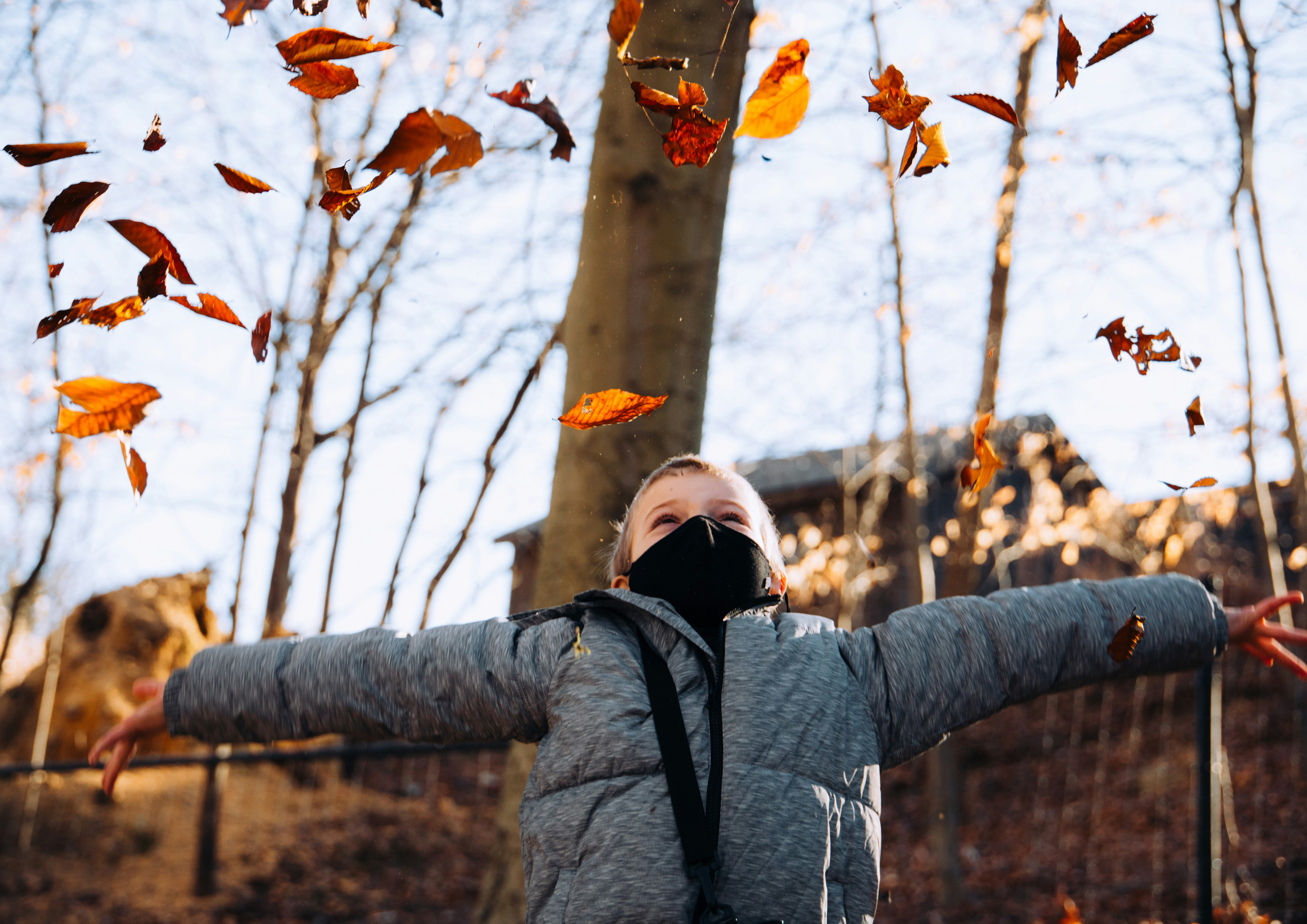 Femme en veste grise couvrant son visage de feuilles brunes