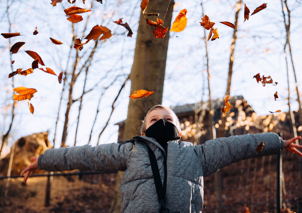 woman in gray jacket covering her face with brown leaves