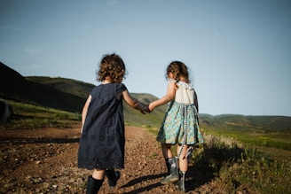 2 girls in blue dress standing on brown field during daytime
