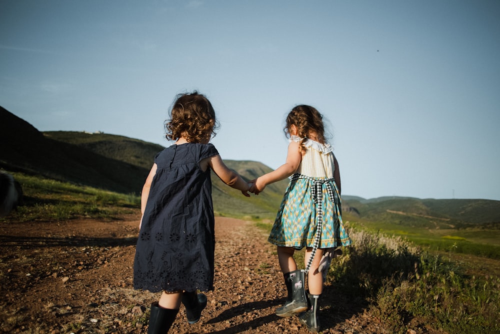 2 girls in blue dress standing on brown field during daytime