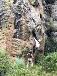 Instructor demonstrating proper belaying technique on a natural rock face.