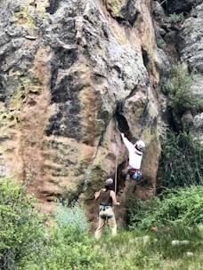 Instructor demonstrating proper belaying technique on a natural rock face.