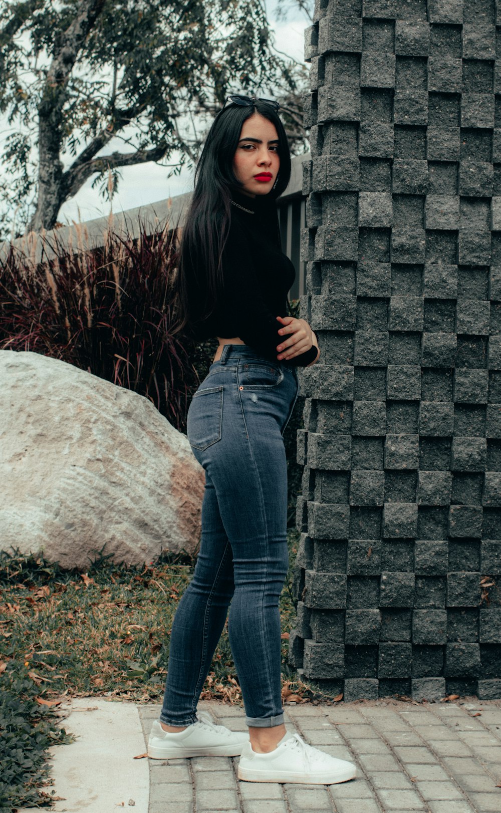 woman in black long sleeve shirt and blue denim jeans standing beside gray concrete wall during
