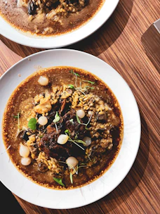 A steaming bowl of gumbo with rich, dark roux and colorful vegetables, set against a backdrop of a bayou sunset.