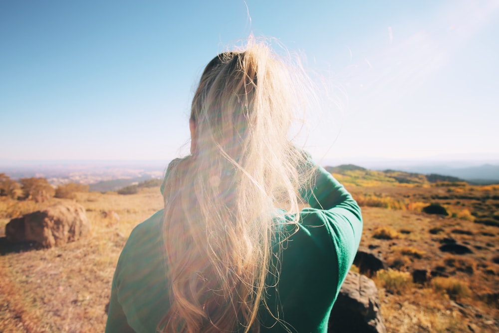 woman in green jacket sitting on brown rock during daytime