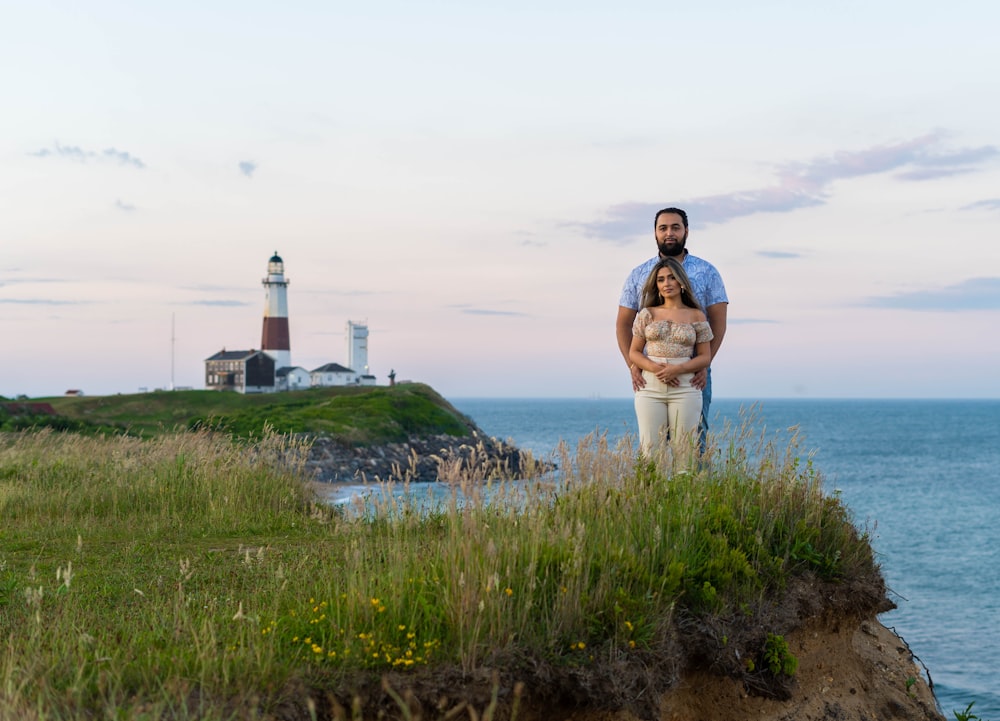 homme en chemise à carreaux marron et blanc debout sur le champ d’herbe verte près du phare blanc