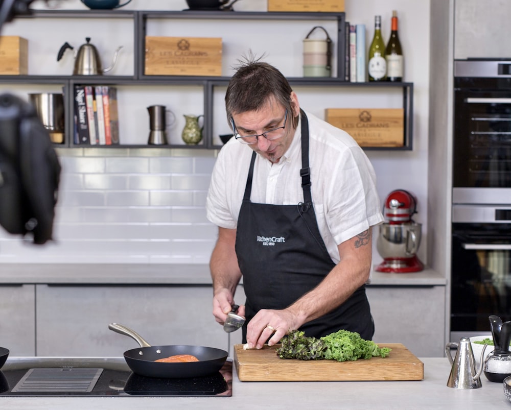 man in black apron slicing green vegetable