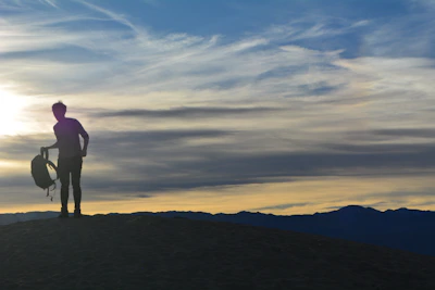 Sunset view with a silhouette of a person carrying a hiking backpack on a hilltop